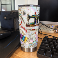 A custom name tumbler with sewing machine design stands upright on a wooden desk next to a computer keyboard.