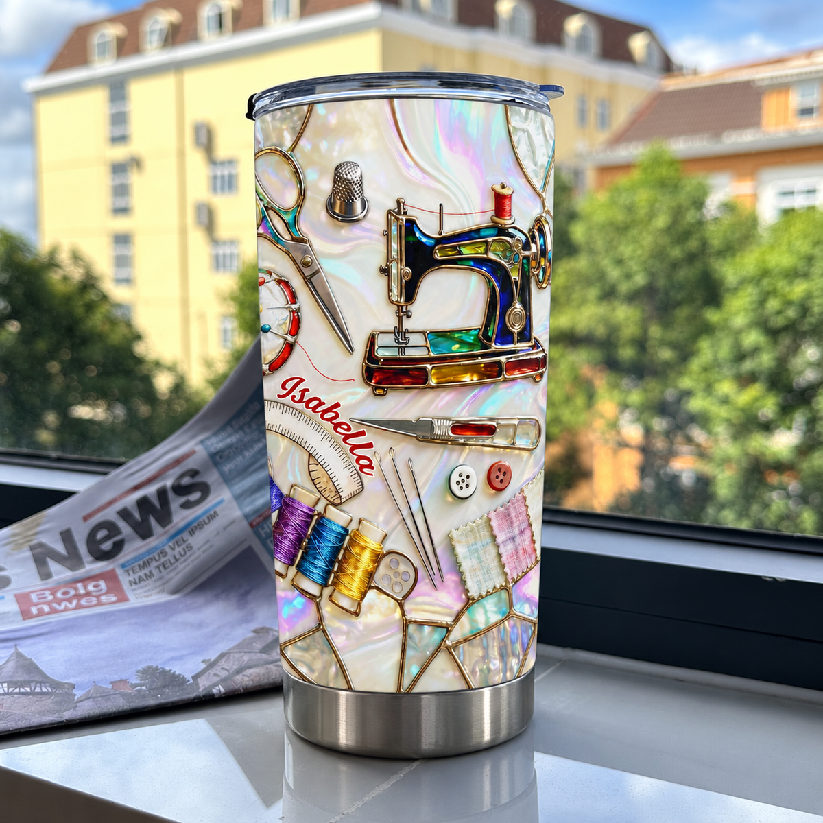 Custom name tumbler with sewing machine design placed on a windowsill with a blurred building and trees in the background.