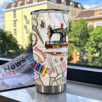 Custom name tumbler with sewing machine design placed on a windowsill with a blurred building and trees in the background.
