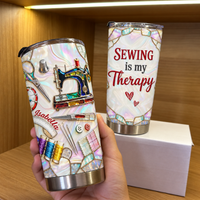 Hand holding a custom name tumbler featuring a vintage sewing machine design, with a second tumbler on a box behind it.