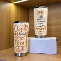 Two custom vanity design tumblers on a wooden shelf, featuring makeup graphics, pearls, and a personalized name.