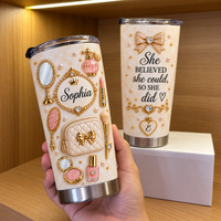 Hand holding custom gold and pearl vanity tumbler with name Sophia, next to matching quote tumbler on a white box.