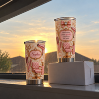 Personalized hair stylist gift tumbler with rose gold chair design standing on white box in front of window during sunset.