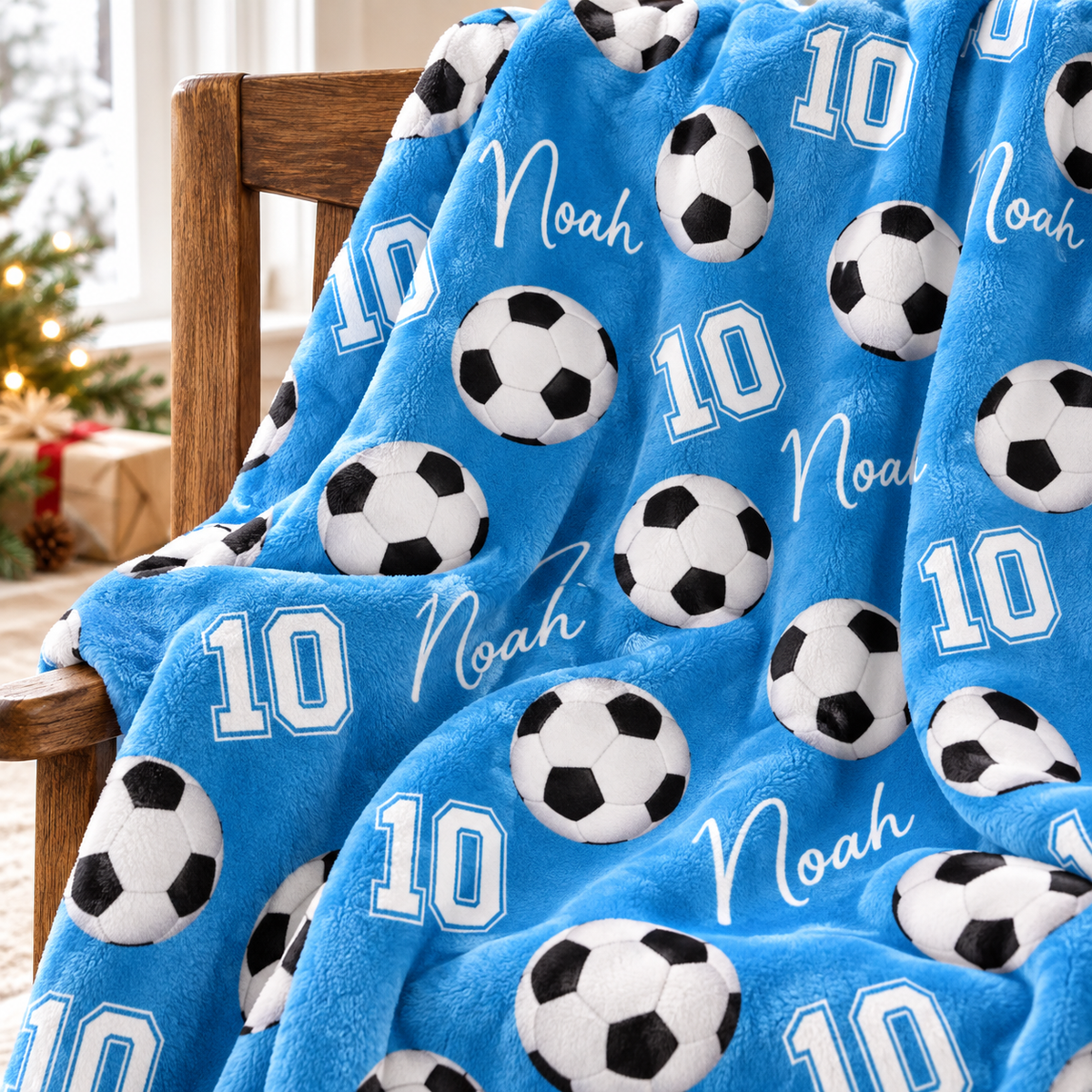 A sky blue soccer ball pattern blanket with name Noah and number 10 draped over a wooden chair.