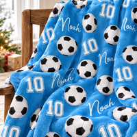 A sky blue soccer ball pattern blanket with name Noah and number 10 draped over a wooden chair.