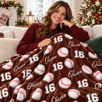 A woman smiles holding a brown baseball pattern blanket with name Oliver and number 16 on a sofa.
