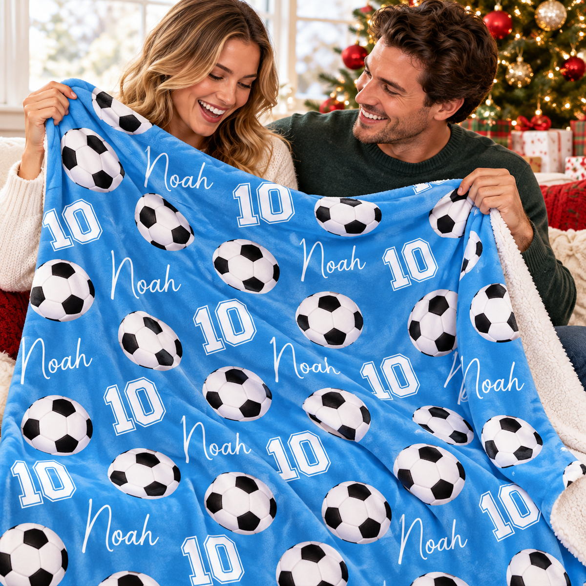 A couple holds up a custom blue soccer ball pattern blanket featuring the name Noah and number 10.
