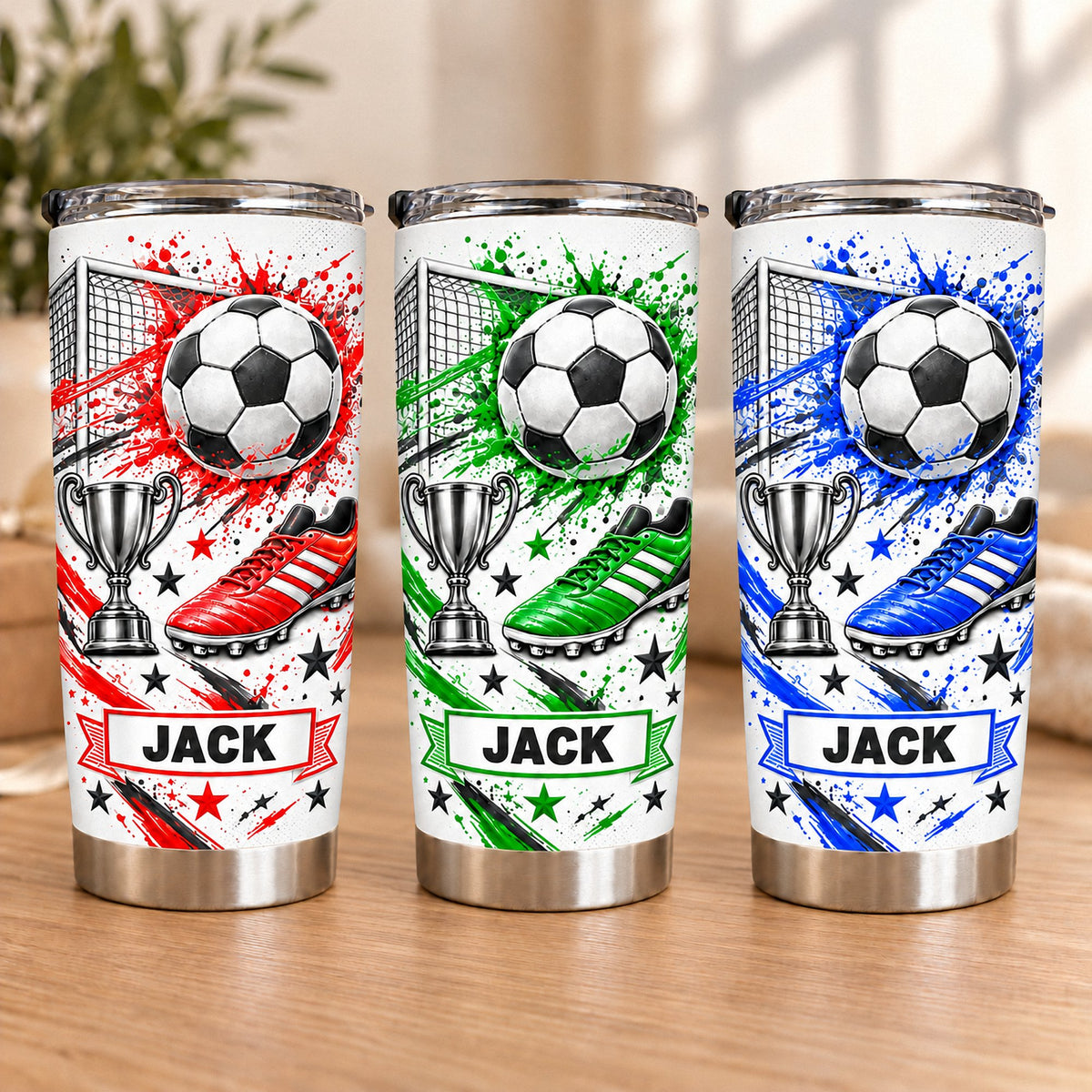 Three personalized stainless steel soccer tumblers displaying red, green, and blue splatter graphics with the custom name