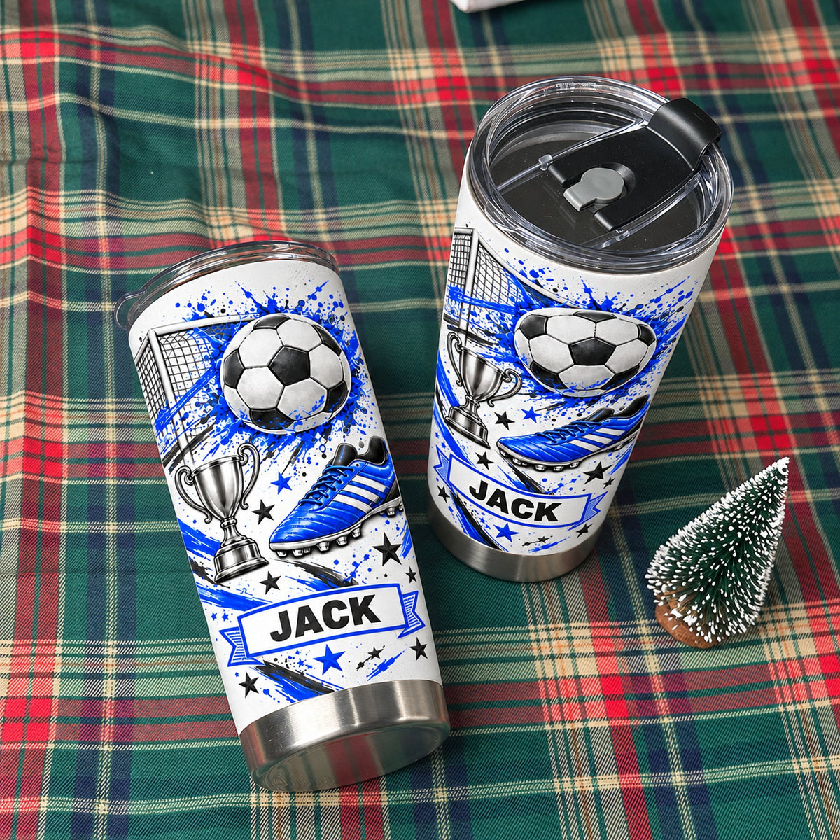 Two blue soccer tumbler personalized custom name cups with blue splatter graphics and black lids standing on plaid fabric.