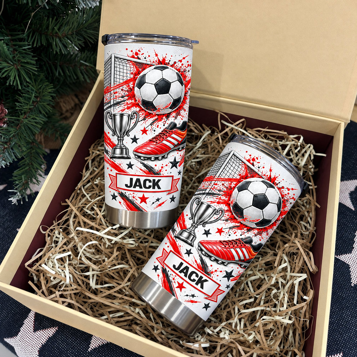 Two soccer tumbler personalized custom name cups packed inside an open gift box filled with shred paper and pine tree decor.