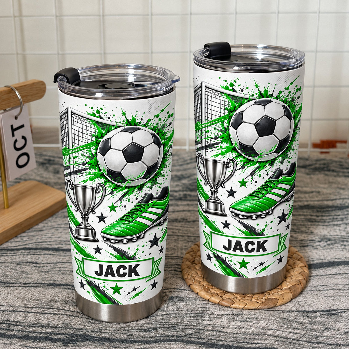 Two green soccer tumbler personalized custom name cups with black lids displayed against a white tiled wall.