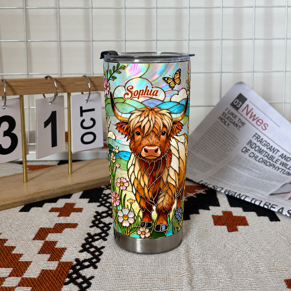 Scottish highlander cup with custom name resting on patterned cloth next to October calendar and open newspaper.