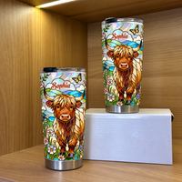 Two stainless steel tumbler cups featuring stained glass Highland cow and custom name banner on wooden shelf with white box.