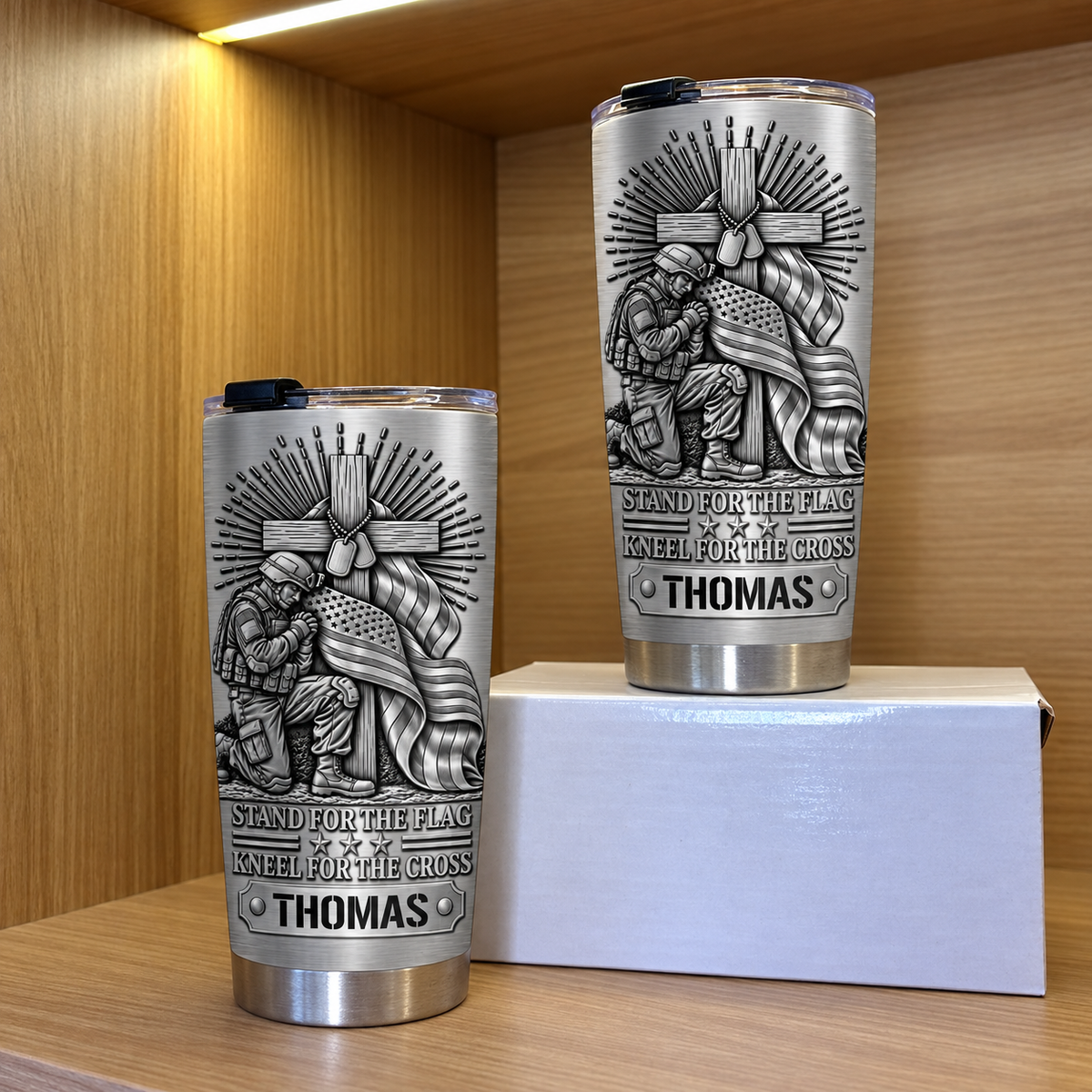 Two Christian patriotic tumblers on a wooden shelf next to a small white box.