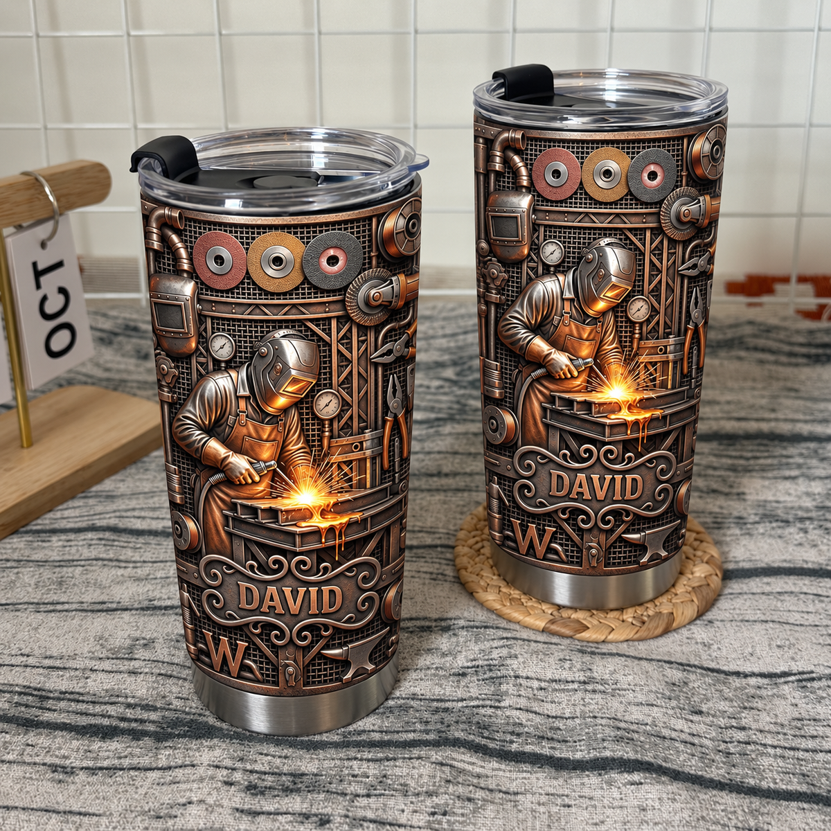 Two custom name welder tumblers displayed on wooden shelf with white grid wall behind.