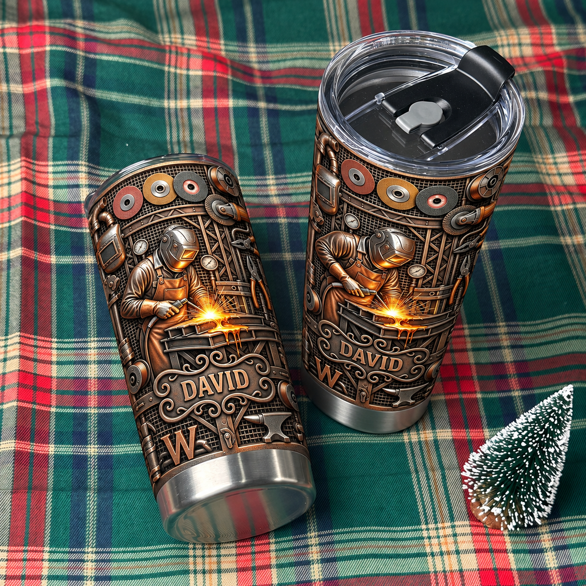 Two stainless steel travel tumblers with welder design resting on green and red plaid fabric.
