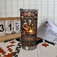 Custom name welder tumbler standing on patterned rug next to wooden calendar and newspaper.