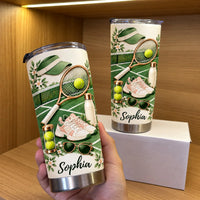 Hand holding a personalized tennis cup tumbler next to a second tumbler and white box on a shelf.