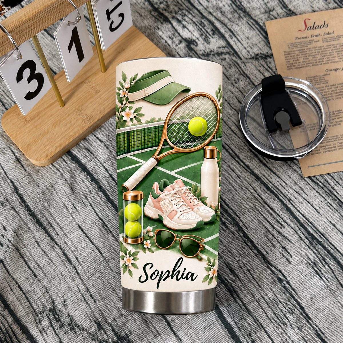 Personalized tennis lover gift tumbler standing on a rustic wooden table with its detached splash-proof lid.