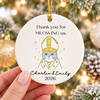 Hand holding personalized round ceramic ornament featuring a grey cat in bishop vestments and gold accents.
