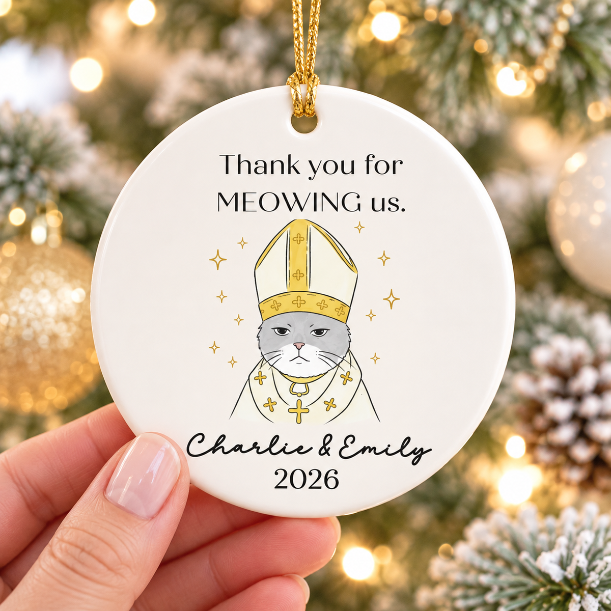 Hand holding personalized round ceramic ornament featuring a grey cat in bishop vestments and gold accents.