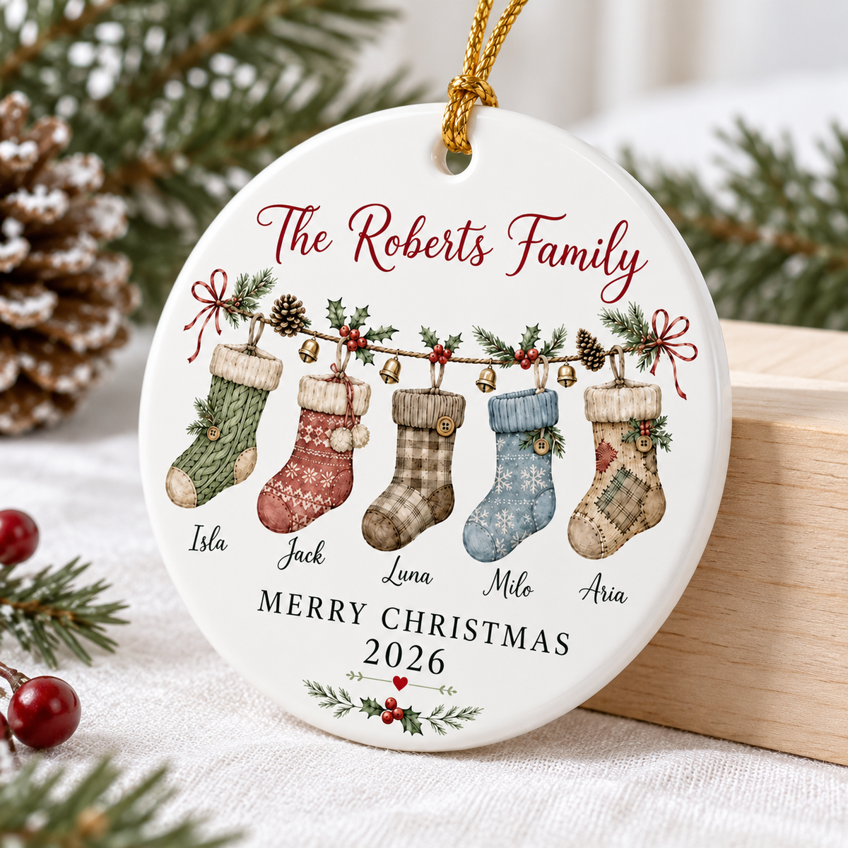Close-up of a personalized family ornament hanging near a pine cone and holiday greens.