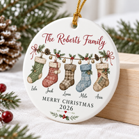 Close-up of a personalized family ornament hanging near a pine cone and holiday greens.