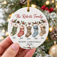 A hand holding the flat ceramic family stocking ornament against a backdrop of festive holiday lights.