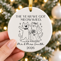Hand holding the personalized ceramic cat wedding ornament against a tree background.