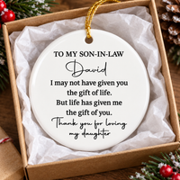 Ceramic Christmas ornament for son in law resting inside an open gift box lined with white tissue paper.