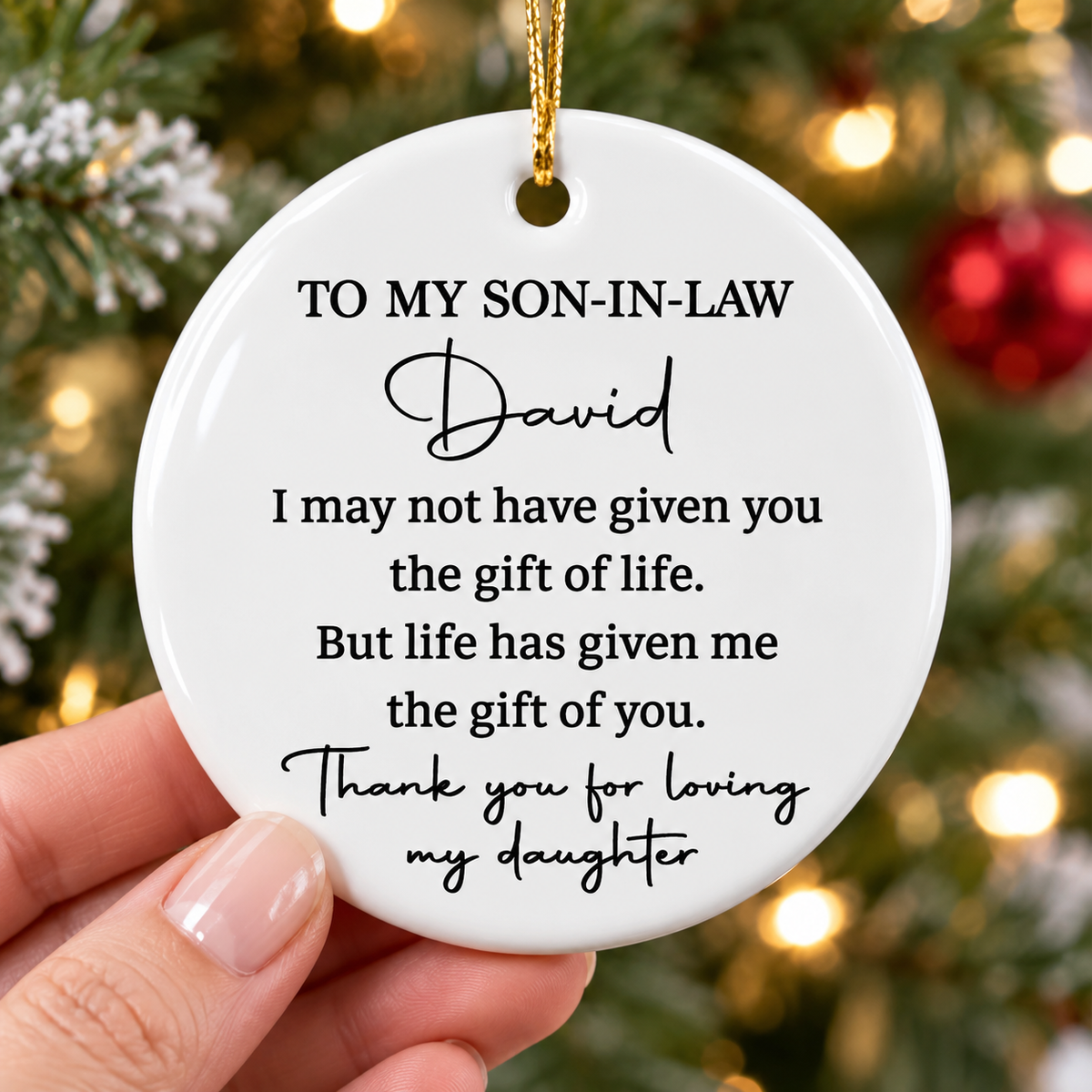 Mother holding a custom ceramic Christmas ornament for son in law against a festive tree background.