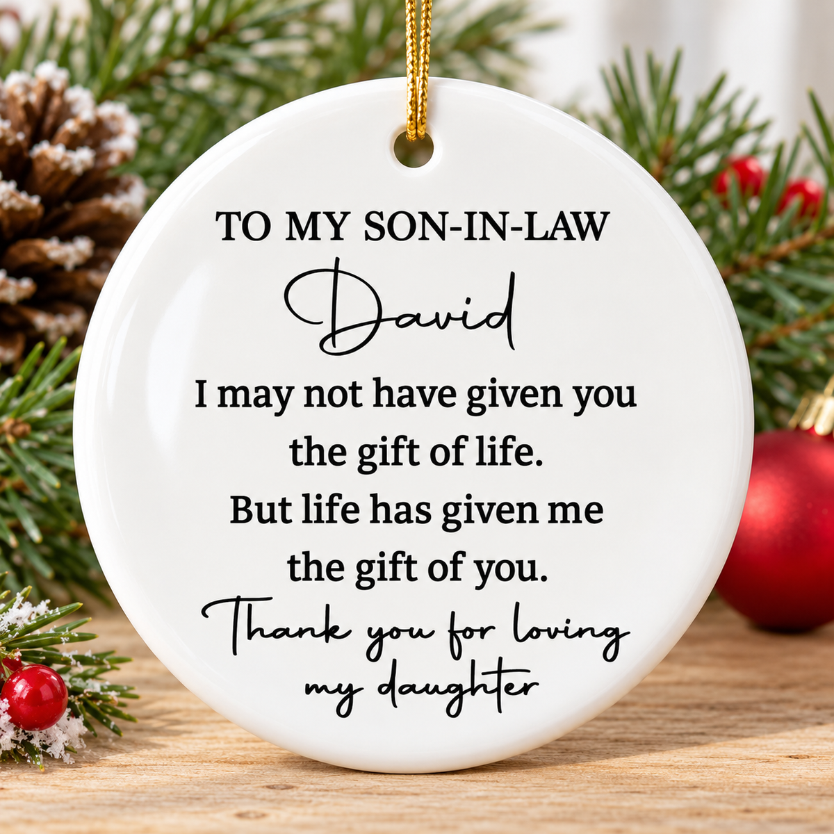 Two-sided ceramic ornament for son in law displayed on a wooden surface with pinecones and red berries.