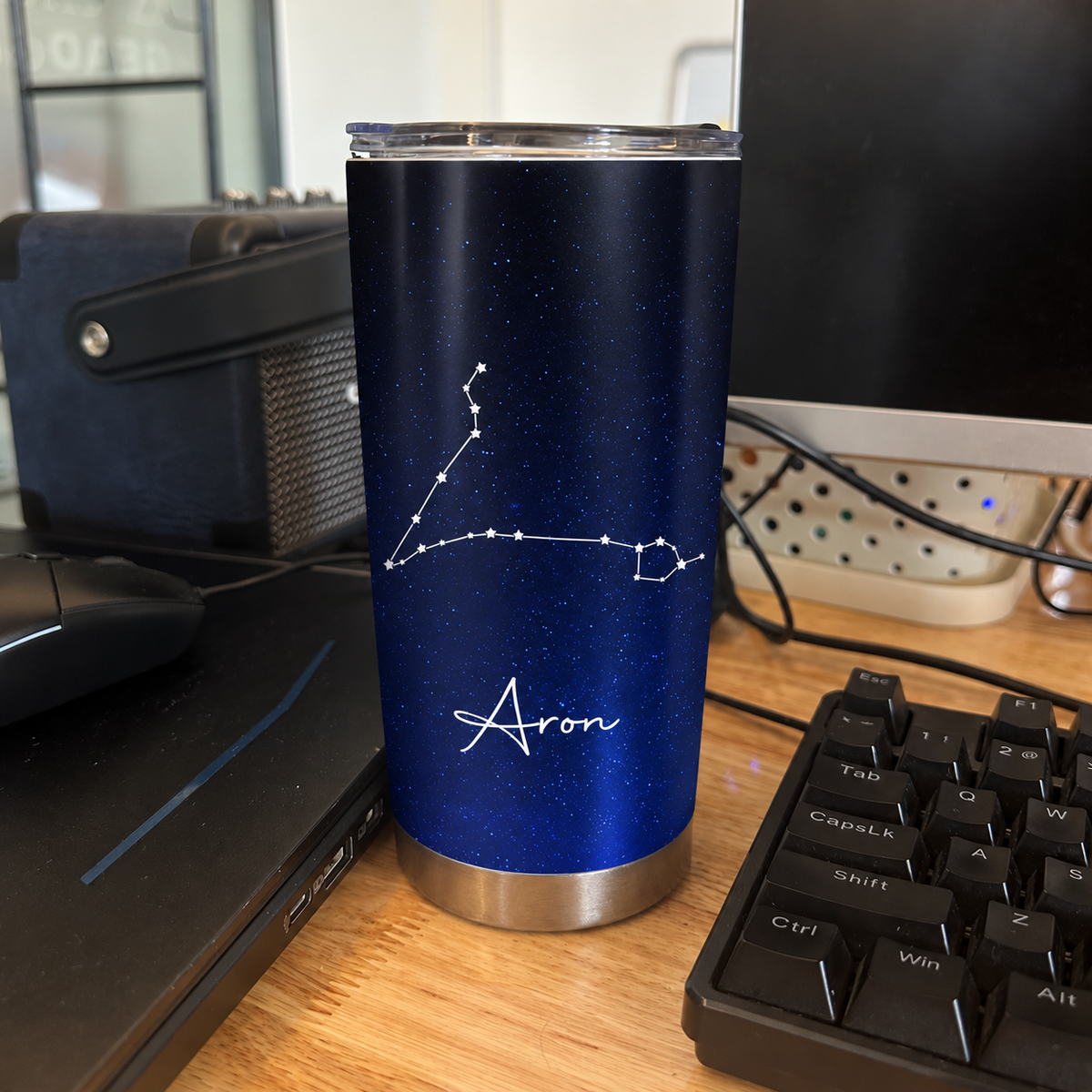 A single stainless steel tumbler with name Aron and constellation art sits on a desk next to a keyboard.