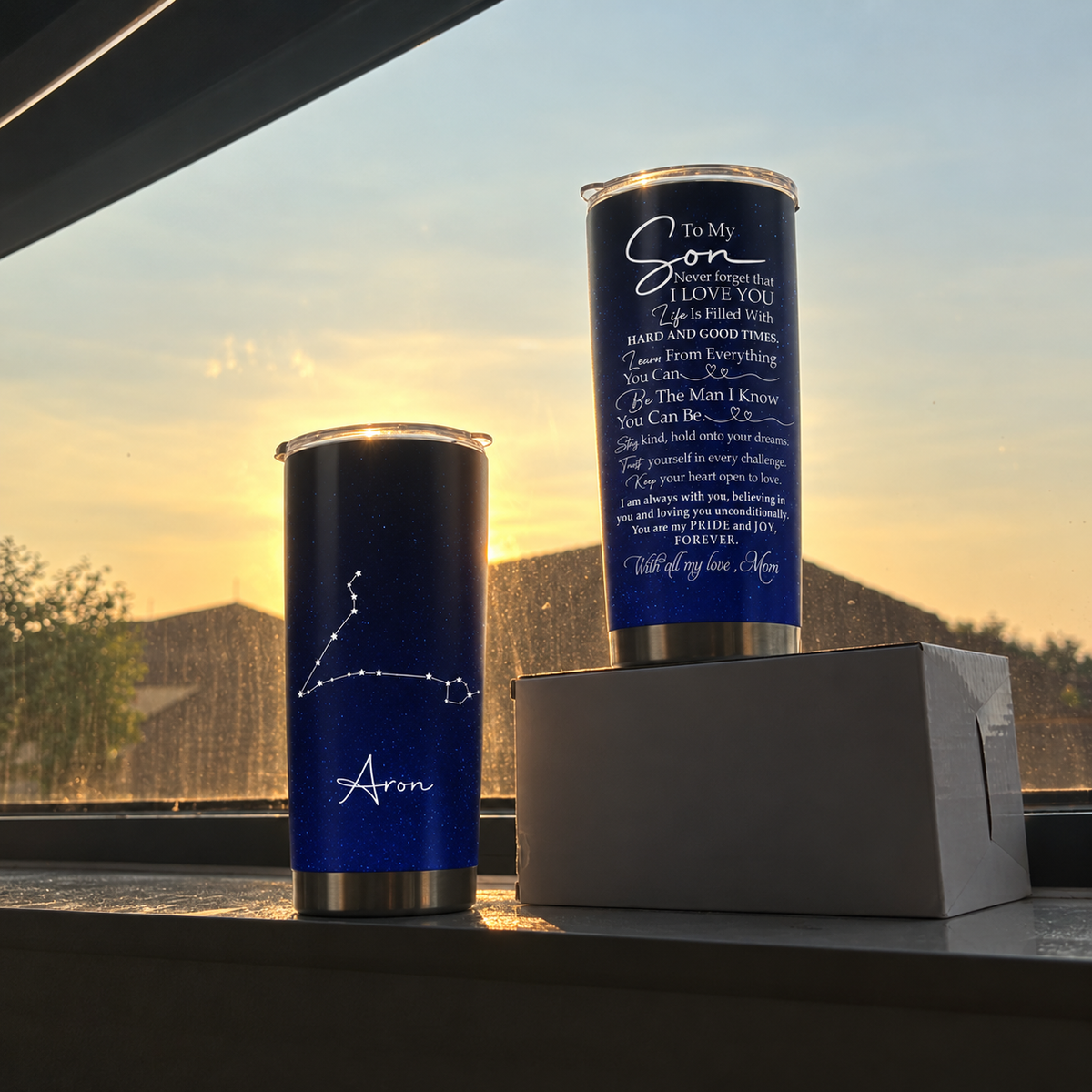 Two stainless steel tumbler cups with starry galaxy prints sit on a windowsill against a glowing sunset background.