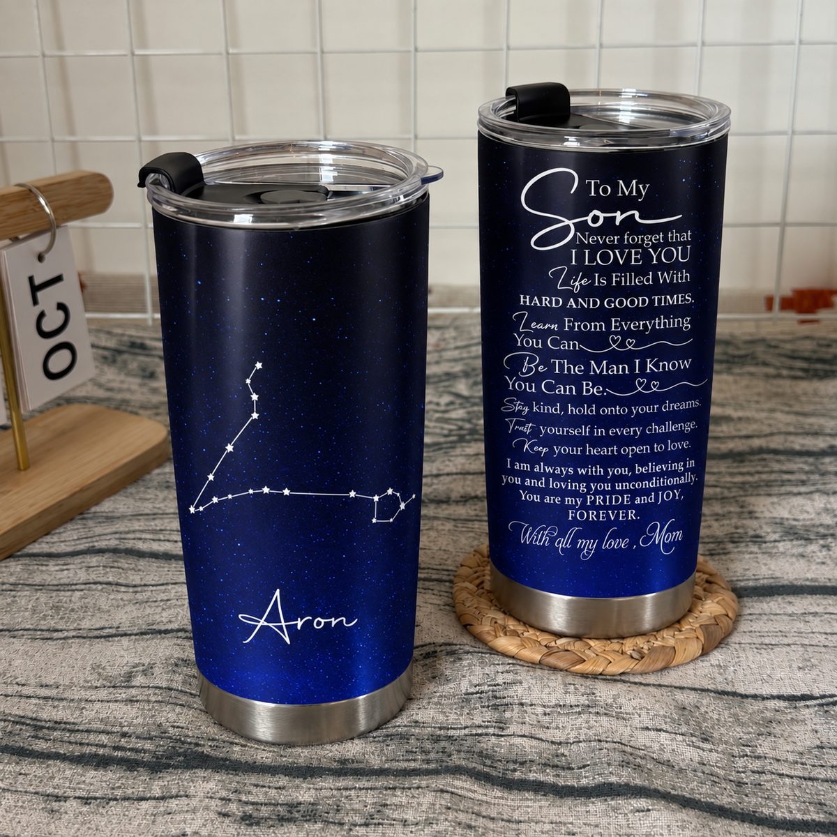 Two stainless steel tumblers with son birthday gift quote and constellation design stand on a wooden surface.