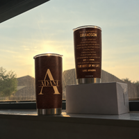 Two To My Wonderful Grandson tumblers on a windowsill against a sunset sky, showing monogram and quote sides.