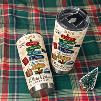 Two stainless steel travel tumblers with a vintage travel signpost design resting on a red and green plaid fabric next to a