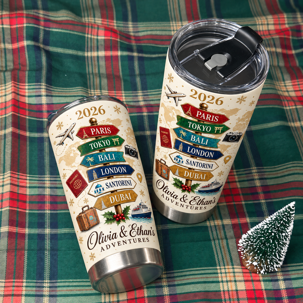 Two stainless steel travel tumblers with a vintage travel signpost design resting on a red and green plaid fabric next to a