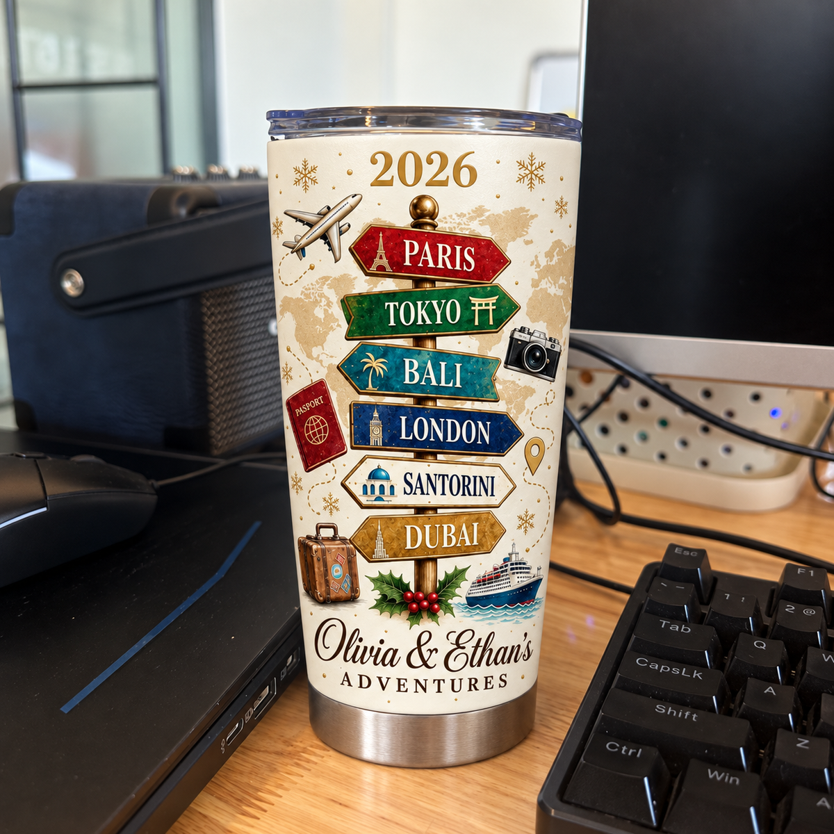A custom stainless steel travel tumbler featuring a vintage travel signpost and couple names on a wooden desk near a