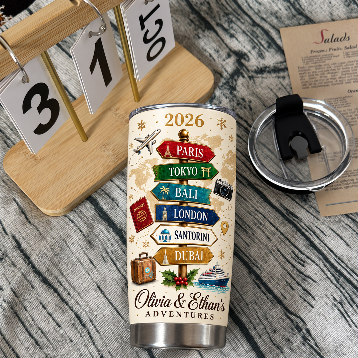 A custom couple adventure mug with a travel signpost graphic resting on a table beside a wooden calendar and cup lid.