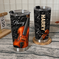 Two personalized violin tumblers with black backgrounds, staff lines, and custom names resting on a textured surface.