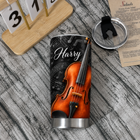 Personalized violin insulated travel mug with sheet music design and clear lid beside a calendar on a wooden table.