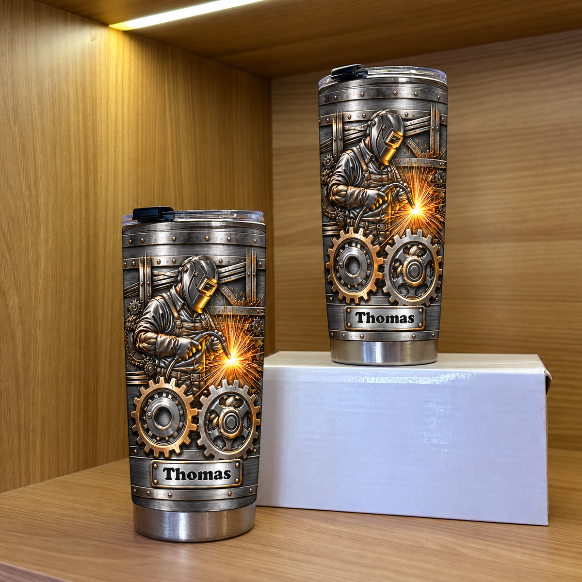 Two personalized stainless steel welder tumblers displayed upright on a wooden shelf.