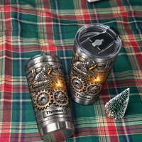 Two steampunk welder tumblers with custom names displayed on a green plaid blanket next to a tiny tree.