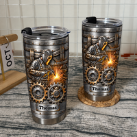 Two vacuum-insulated stainless steel welder tumblers with a steampunk gear design on a rustic textured surface.