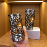A hand holding a personalized stainless steel welder tumbler with a matching tumbler resting on a white box.