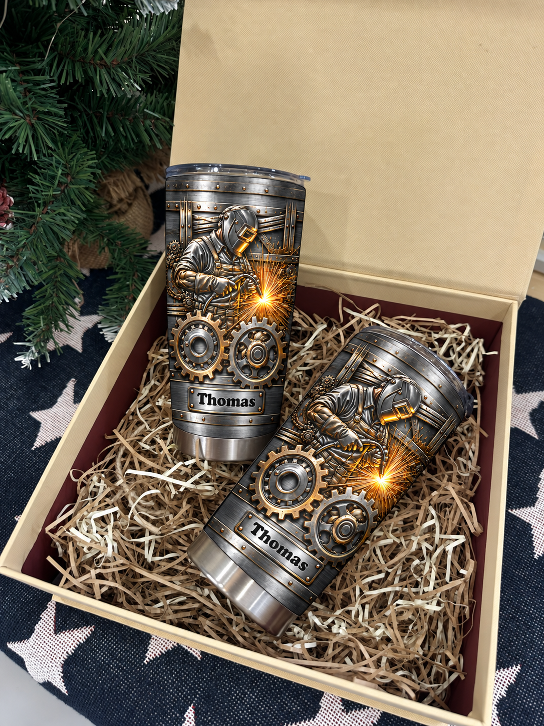 Two custom stainless steel welder tumblers with gears in a gift box with shredded paper, near a tree.