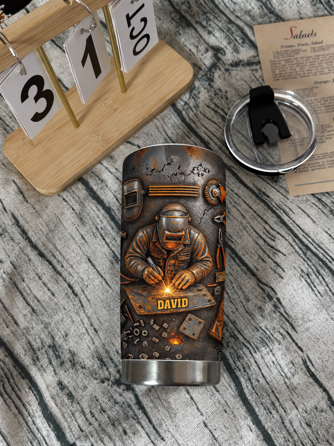 Welder personalized tumbler with custom name lying on a wooden surface next to a calendar.