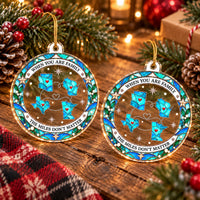 Two round clear acrylic long distance Christmas ornaments hanging on a pine tree branch with red berries.
