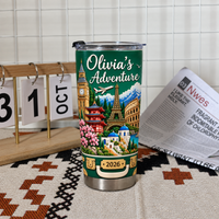 Trip memory keepsake tumbler featuring landmarks on a table next to a wooden desk calendar and a newspaper.